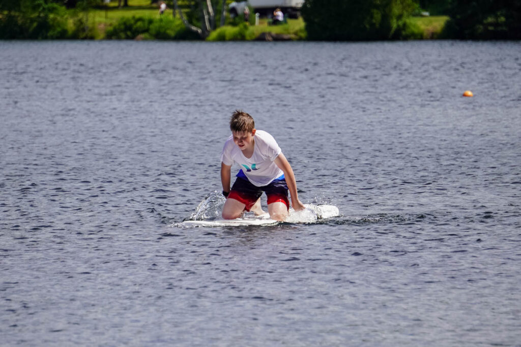 Brady paddles on the lake while kneeling on a surfboard.